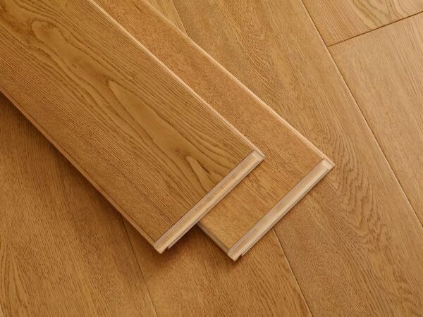 Close-up of laminate flooring planks in a warm oak finish, featuring realistic wood grain patterns, a natural wood-look texture, and visible interlocking edges.